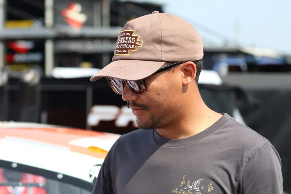 Brad Perez in a t-shirt and hat standing in front of his race car.