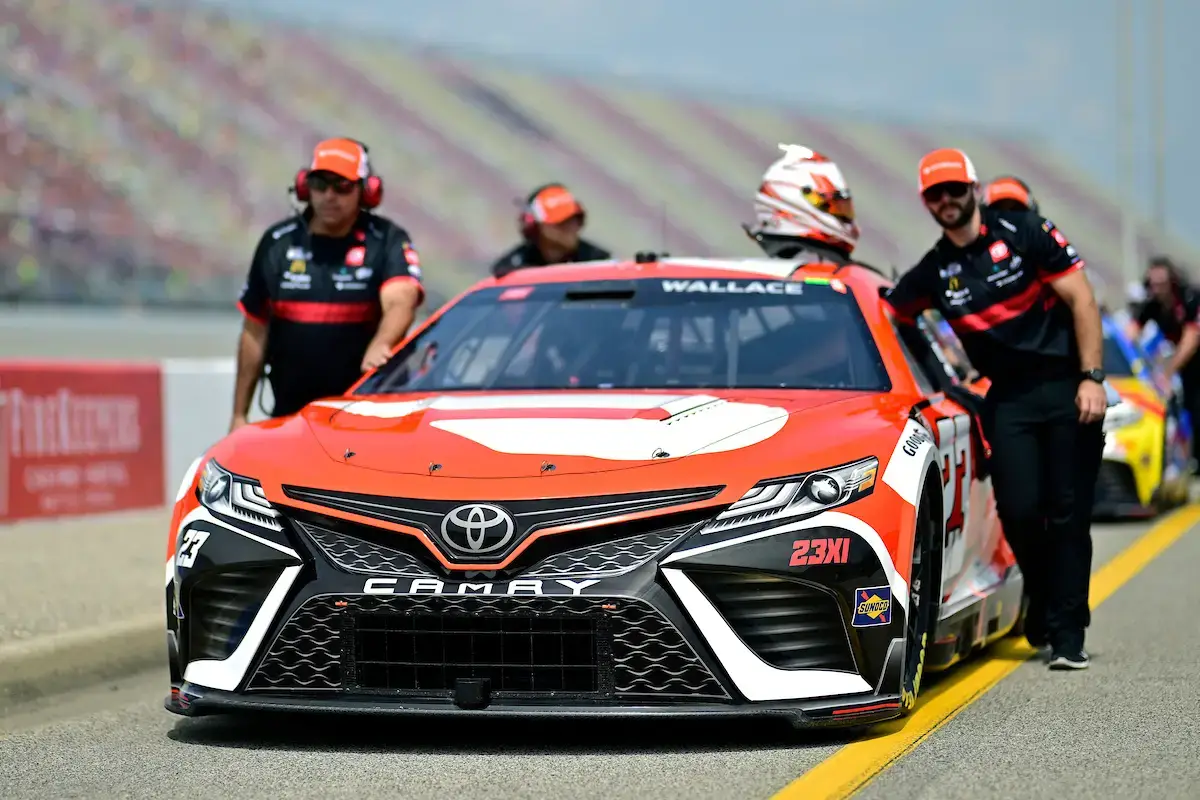 Bubba Wallace's crew pushes his white and red DoorDash car down pit road at Michigan International Speedway.