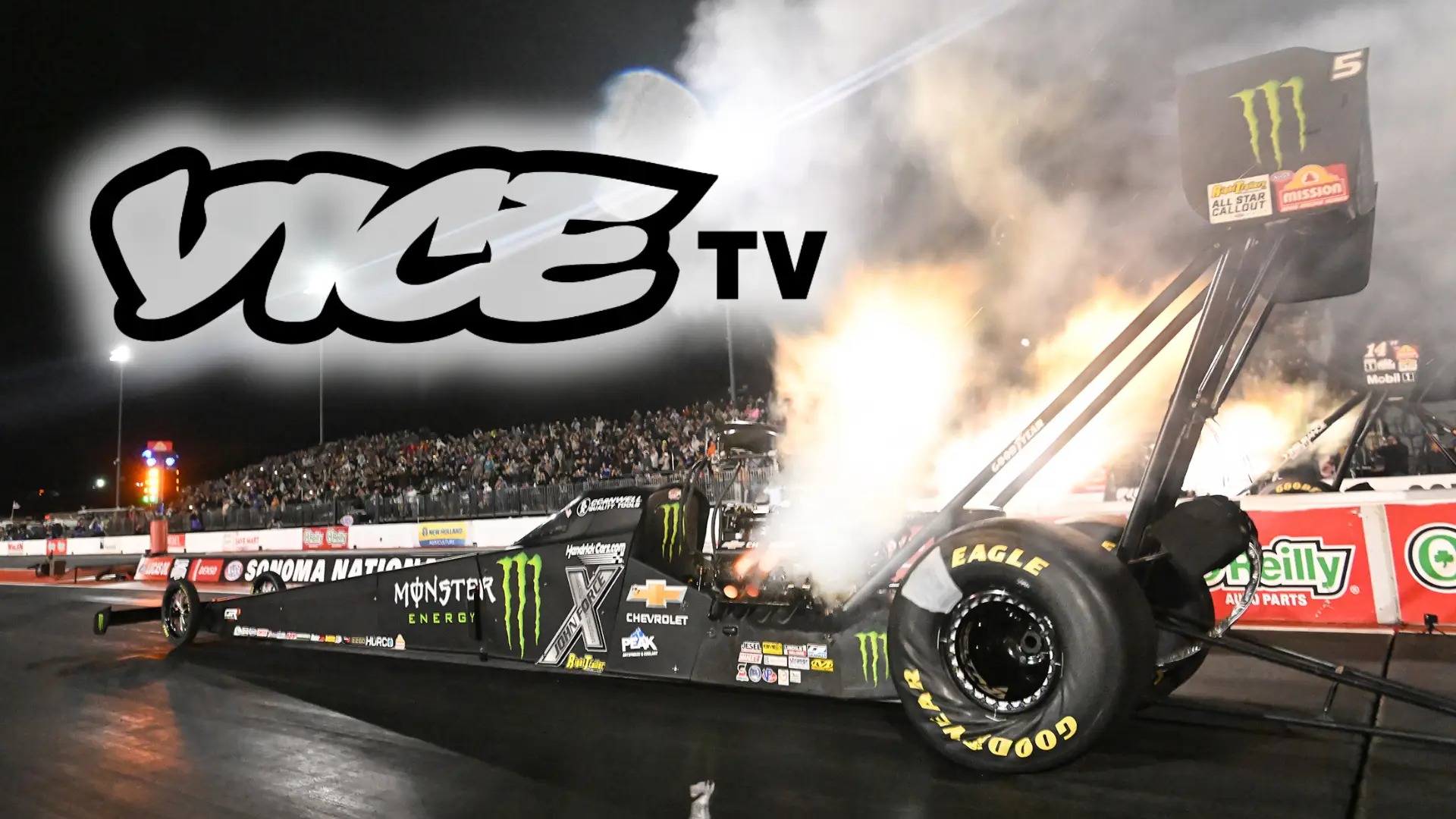 Brittany Force's Top Fuel Dragster with smoke and fire coming out the pipes going down the drag strip at night.
