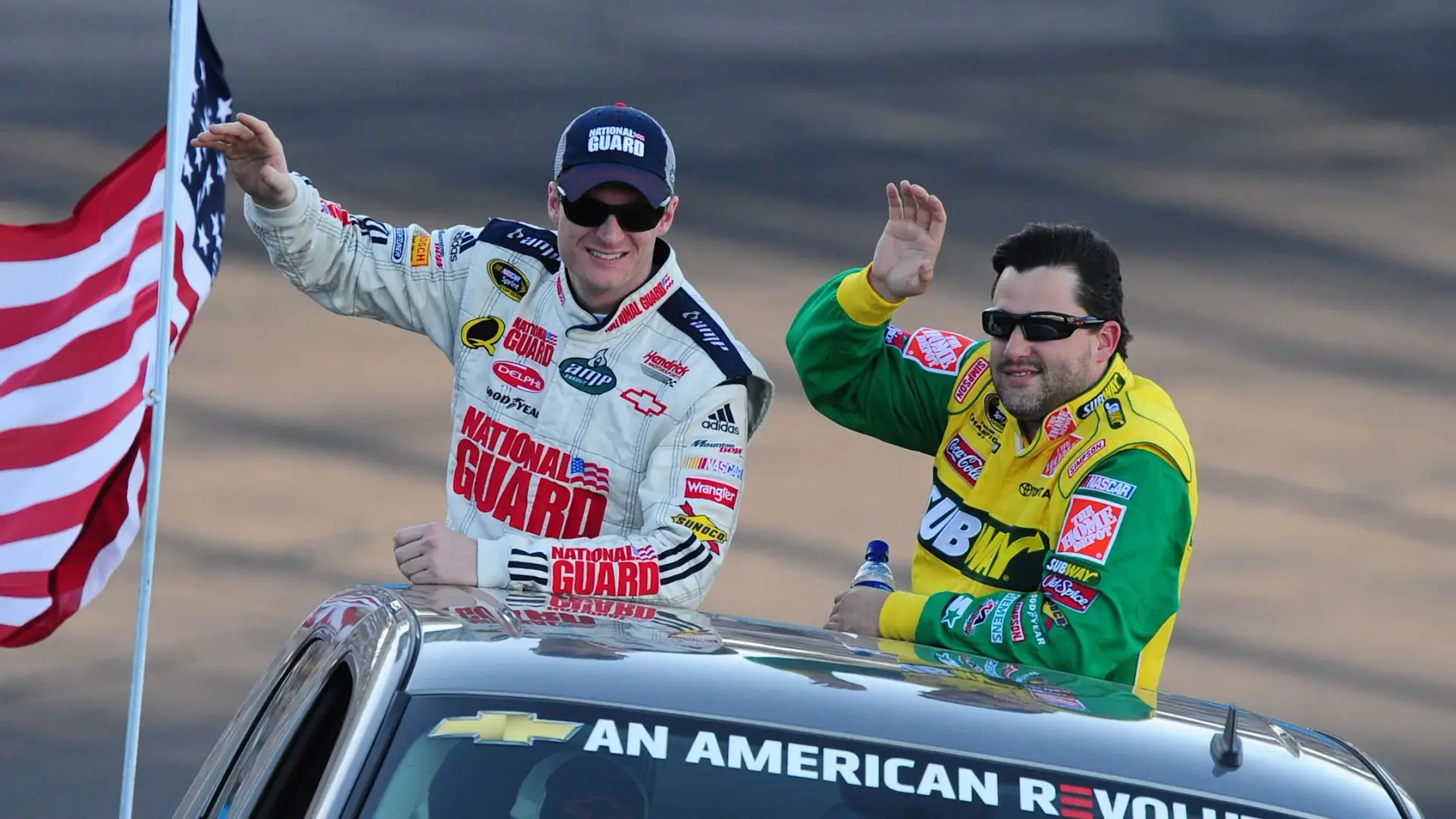 Tony Stewart and Dale Earnhardt Jr. circa 2008 riding on a pace truck together around the race track for driver intros. Both drivers are waving to fans.
