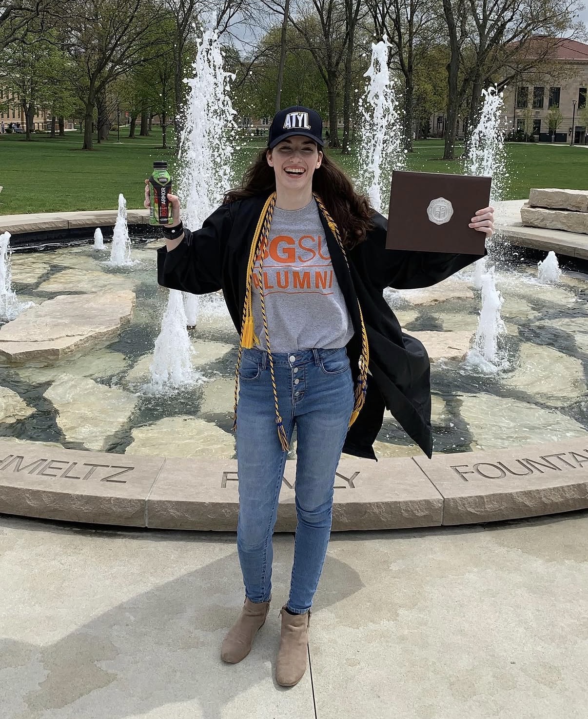 Taylor wears her college graduation gown, holding her diploma in one hand and a BodyArmor in another after graduation from BGSU in 2023. (Photo Credit: Taylor Kitchen)